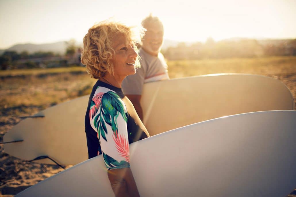 Two seniors on the beach with surfboards, a smiling, attractive man and woman