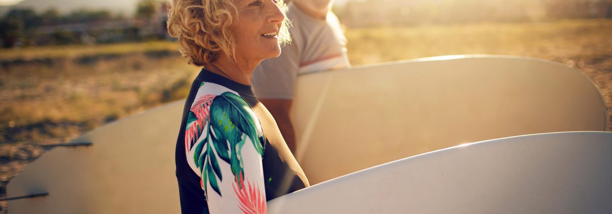 Two seniors on the beach with surfboards, a smiling, attractive man and woman